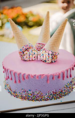 Ein rosa und lila Tropfkuchen mit Waffelkegel mit Streuseln darauf - vertikaler Schuss Stockfoto