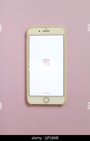 Eine vertikale Nahaufnahme eines iPhone mit dem Instagram-Logo auf dem Bildschirm vor rosa Hintergrund Stockfoto