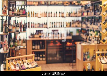 Weinladen mit Weinflaschenregalen. Abstrakter, warm getönter defokussierter Hintergrund Stockfoto