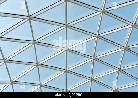 Architektonische Glasstruktur mit geometrischem Dreiecksmuster auf blauem Himmel. Stahlglas Dachwandkonstruktion transparentes Fenster mit Stockfoto