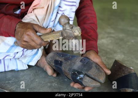 Traditioneller Schuhmacher mit Hammer, der handgefertigte Schuhe zum Verkauf herstellt. Nahaufnahme von Menschenhänden, die auf Leder klopfen, genagelt mit einem Holzrahmen namens la Stockfoto