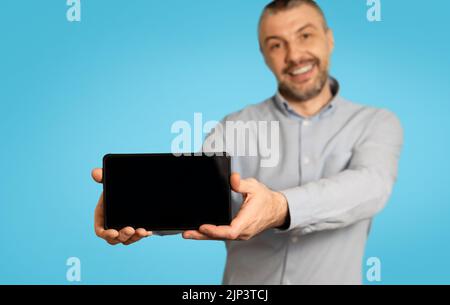 Fröhlicher Mann, Der Mobiltelefon Mit Leerem Bildschirm Und Blauem Hintergrund Zeigt Stockfoto