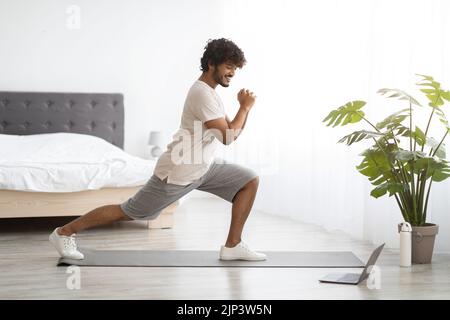 Sportlicher indischer Mann in Sportbekleidung, der zu Hause mit einem Laptop trainiert Stockfoto