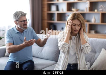 Traurig verärgert wütend erwachsenen europäischen Ehemann brüllt unglückliche Frau, bedeckt Ohren im Wohnzimmer Interieur Stockfoto