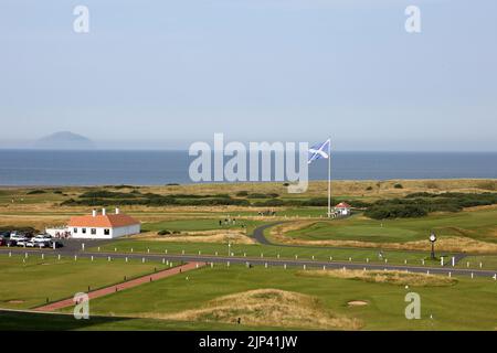 Trump Turnberry, Ayrshire, Schottland Großbritannien.eine der größten Saltire-Flaggen in Schottland dominiert die Gegend und kann von Meilen entfernt gesehen werden. Dieser Blick vom Hotel Turnberry mit der Starterhütte für den ersten Tee, Übungsgreens und das 18. Green. Ebenfalls auf dem Foto ist die ikonische große Uhr zu sehen, die den Namen Donald Trumps trägt. Am Horizont steht Ailsa Craig im Firth of Clyde Stockfoto