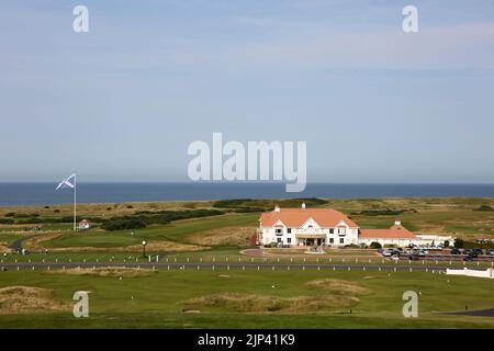 Trump Turnberry, Ayrshire, Schottland Großbritannien.eine der größten Saltire-Flaggen in Schottland dominiert die Gegend und kann von Meilen entfernt gesehen werden. Dieser Blick vom Hotel Turnberry mit der Starterhütte für den ersten Tee, Übungsgreens und das 18. Green. Ebenfalls auf dem Foto ist die ikonische große Uhr zu sehen, die Donald Trumps Namen trägt. Das Gebäude auf dem Foto ist das Clubhaus Stockfoto