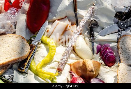 Rumänische traditionelle Küche mit Würstchen, Zwiebeln und Käse, Schinken und Paprika und einem Messer auf einem Handtuch Stockfoto