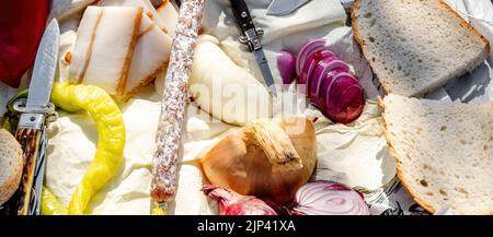 Rumänische traditionelle Küche mit Würstchen, Zwiebeln und Käse, Schinken und Paprika und einem Messer auf einem Handtuch Stockfoto