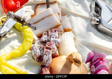 Rumänische traditionelle Küche mit Würstchen, Zwiebeln und Käse, Schinken und Paprika und einem Messer auf einem Handtuch Stockfoto