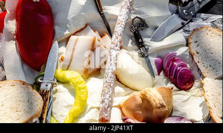 Rumänische traditionelle Küche mit Würstchen, Zwiebeln und Käse, Schinken und Paprika und einem Messer auf einem Handtuch Stockfoto