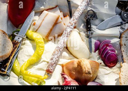 Rumänische traditionelle Küche mit Würstchen, Zwiebeln und Käse, Schinken und Paprika und einem Messer auf einem Handtuch Stockfoto