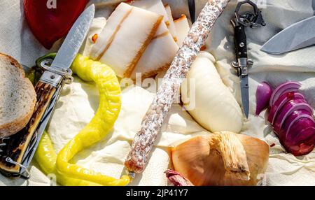 Rumänische traditionelle Küche mit Würstchen, Zwiebeln und Käse, Schinken und Paprika und einem Messer auf einem Handtuch Stockfoto