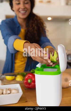 Glückliche Birazial Frau, die Lebensmittel kompostiert Gemüseabfälle in der Küche vorbereitet Stockfoto