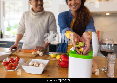 Glückliches biracial Paar, das Essen zubereitet und Gemüseabfälle in der Küche kompostiert Stockfoto