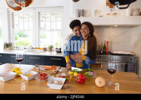 Glückliches biracial Paar, das Essen zubereitet und in der Küche umarmt Stockfoto