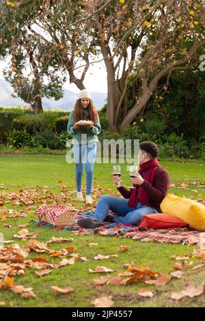 Vertikales Bild eines glücklichen, vielfältigen Paares, das im Herbstpark picknickt Stockfoto