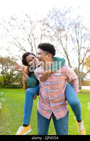 Glückliches biracial Paar mit Spaß Huckepack im Garten und lachen Stockfoto