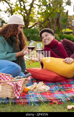 Vertikales Bild eines glücklichen, vielfältigen Paares, das im Herbstpark picknickt Stockfoto
