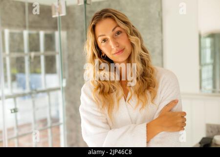 Porträt einer glücklichen kaukasischen Frau in Robe, lächelnd im Badezimmer Stockfoto