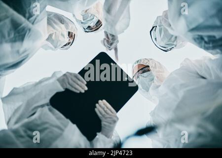 Hazmat Healthcare-Mitarbeiter von unten, die während einer covid Pandemie mit Gesichtsmasken zusammenarbeiten. Team von Ärzten in Quarantäneanzügen diskutieren Stockfoto