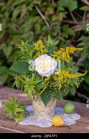 Bouquet von weißen Rosen, Haselnussfrüchten, Goldrute und Holunderbeeren in Vase im Garten Stockfoto