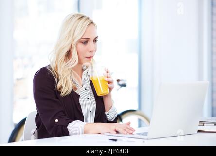 Das Geschäft wird ihrer Reinigung nicht im Weg stehen. Eine attraktive junge Geschäftsfrau trinkt Orangensaft, während sie in ihrem Büro arbeitet. Stockfoto