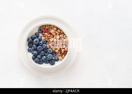 Schüssel mit hausgemachtem Joghurt mit Müsli und Heidelbeeren auf hellem Hintergrund. Draufsicht, Platz für Text kopieren Stockfoto