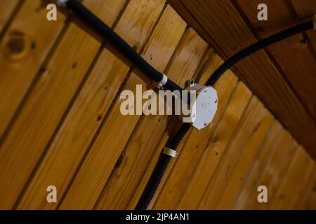 Elektrische Kabel mit Hilfe von durchdringenden hermetischen Klemmen durch die Luft in ein Holzhaus einführen. Stockfoto