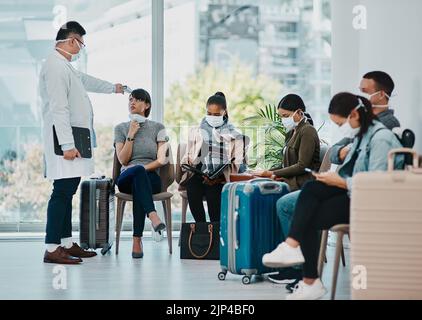 Covid Arzt, der die Temperatur der Reisenden in covid Masken während des Tourismus in einem Flughafen mit einem Infrarot-Thermometer nimmt. Medizinische Fachkraft Stockfoto