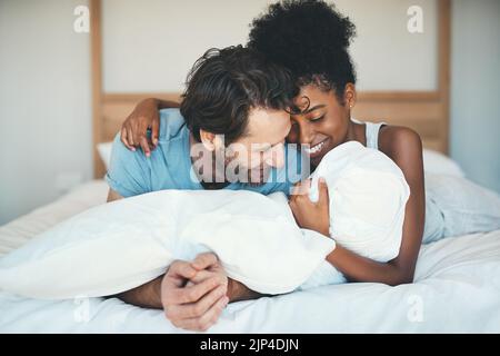 Fun interracial paar lachen, kleben und liegen auf dem Bett in einem Schlafzimmer und sieht glücklich, verliebt und verspielt. Lächelnder Mann und Frau umarmen und Stockfoto