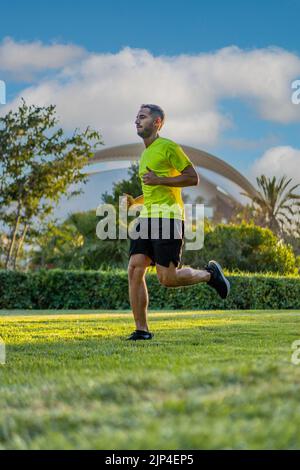 Hispanischer, hübscher Mann mit gelbem T-Shirt beim Joggen bei Sonnenuntergang im Parkgarten der Stadt der Künste und Wissenschaften, Valencia, Spanien. Stockfoto