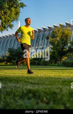 Hispanischer, hübscher Mann mit gelbem T-Shirt beim Joggen bei Sonnenuntergang im Parkgarten der Stadt der Künste und Wissenschaften, Valencia, Spanien. Stockfoto