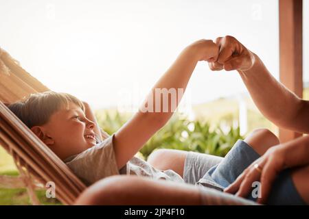 Daddys Junge. Ein unkennbarer Mann und sein kleiner Sohn stoßen mit der Faust, während er draußen auf einer Hängematte liegt. Stockfoto