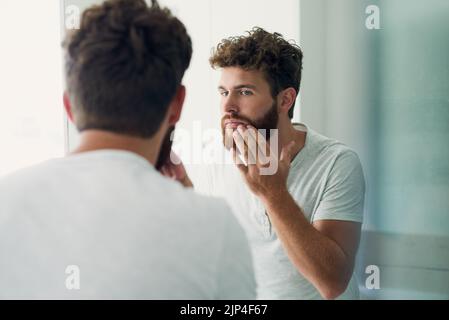 Ein hübscher junger Mann, der seine Haut im Badezimmerspiegel überprüft. Stockfoto