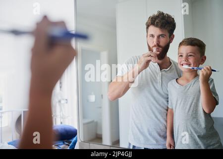 Ein Vater und sein kleiner Sohn putzen ihre Zähne zusammen im Badezimmer zu Hause. Stockfoto