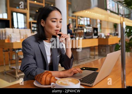 Geschäftige asiatische Geschäftsfrau, die einen Laptop im Café oder Büro benutzt. Stockfoto