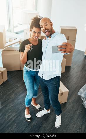 Waren stolz neue Hausbesitzer. Ein junges Paar, das ein Selfie macht, während sie die Schlüssel zu ihrem neuen Zuhause hält. Stockfoto