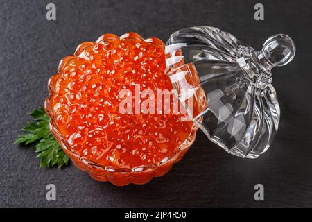 Lachskaviar in einer Kristallschüssel mit Deckel auf schwarzem Hintergrund. Glasplatte voll von Chum Red Kaviar Closeup. Gesalzener Lachsrogen für Gourmet-Food-Konzept Stockfoto