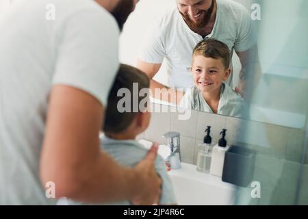 Mein kleiner Junge wird groß und erreicht bereits das Waschbecken. Ein unkennbarer Vater hilft seinem entzückenden kleinen Jungen, sich im Badezimmer die Hände zu waschen Stockfoto