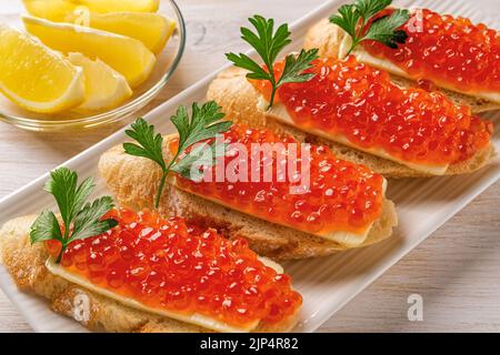 Sandwiches mit rotem Kaviar auf einem weißen Teller. Gourmet-Vorspeise mit Forellenkaviar auf einer Scheibe französischem Baguette mit Butter. Gesalzener Lachsrogen. Stockfoto