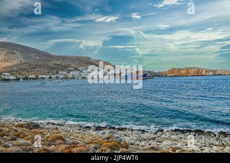 Eine schöne Aussicht auf den felsigen Strand in Folegandros und Karavostasi Hafen mit Booten und weißen Gebäuden Stockfoto