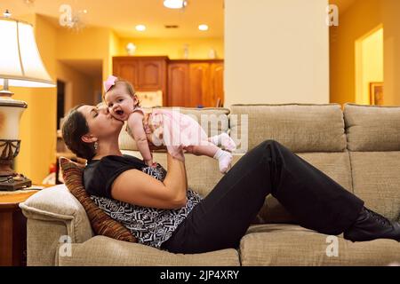 Du wirst immer mein Baby sein. Eine Mutter nimmt ihre entzückende kleine Tochter auf der Couch im Wohnzimmer zu Hause. Stockfoto