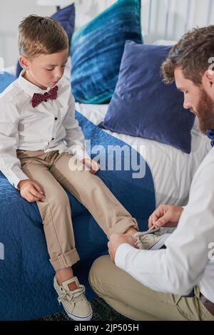 Daddys lehrt mich, wie ich meine Schnürsenkel binden kann. Ein junger, hübscher Vater bindet seine Söhne zu Hause Schnürsenkel. Stockfoto