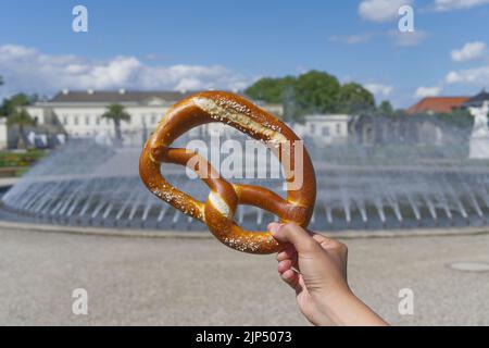 Brezel in der Hand typisches Essen im Garten vor dem Brunnen in Deutschland Europa Stockfoto