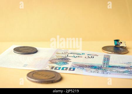 Nahaufnahme einer algerischen Banknote und Münzen auf gelber Oberfläche Stockfoto