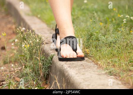 Damenfüße in Sommerschuhen auf der Straße in der Sonne, Damenfüße in Sandalen auf der Straße Stockfoto