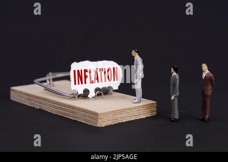 Geschäftsfalle, Krisenkonzept. Figuren von Geschäftsleuten stehen in der Nähe einer Mausefalle, in der der Köder zerrissenes Papier mit der Aufschrift - Inflation ist Stockfoto