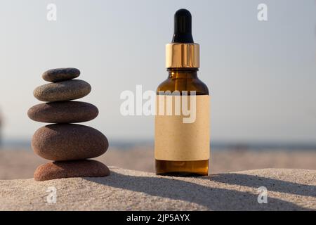 Öl in kleiner brauner Glasflasche am Sandstrand mit Felsen. Natürliche Szene in der Natur. Modell. Stockfoto