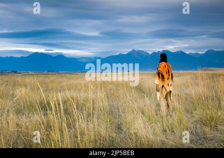 Der gebürtige Amerikaner Blackfeet Nation, gekleidet in ein traditionelles Hemd mit Wildleder und Leggings, steht auf einer Graswiese auf der National Bison Range Stockfoto