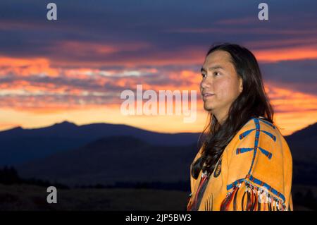 Der junge indianische Mann im traditionellen Hemd aus geperlter Hirschhaut denkt bei einem herrlichen Sonnenuntergang über den Northern Plains, Montana, über seine Zukunft nach Stockfoto